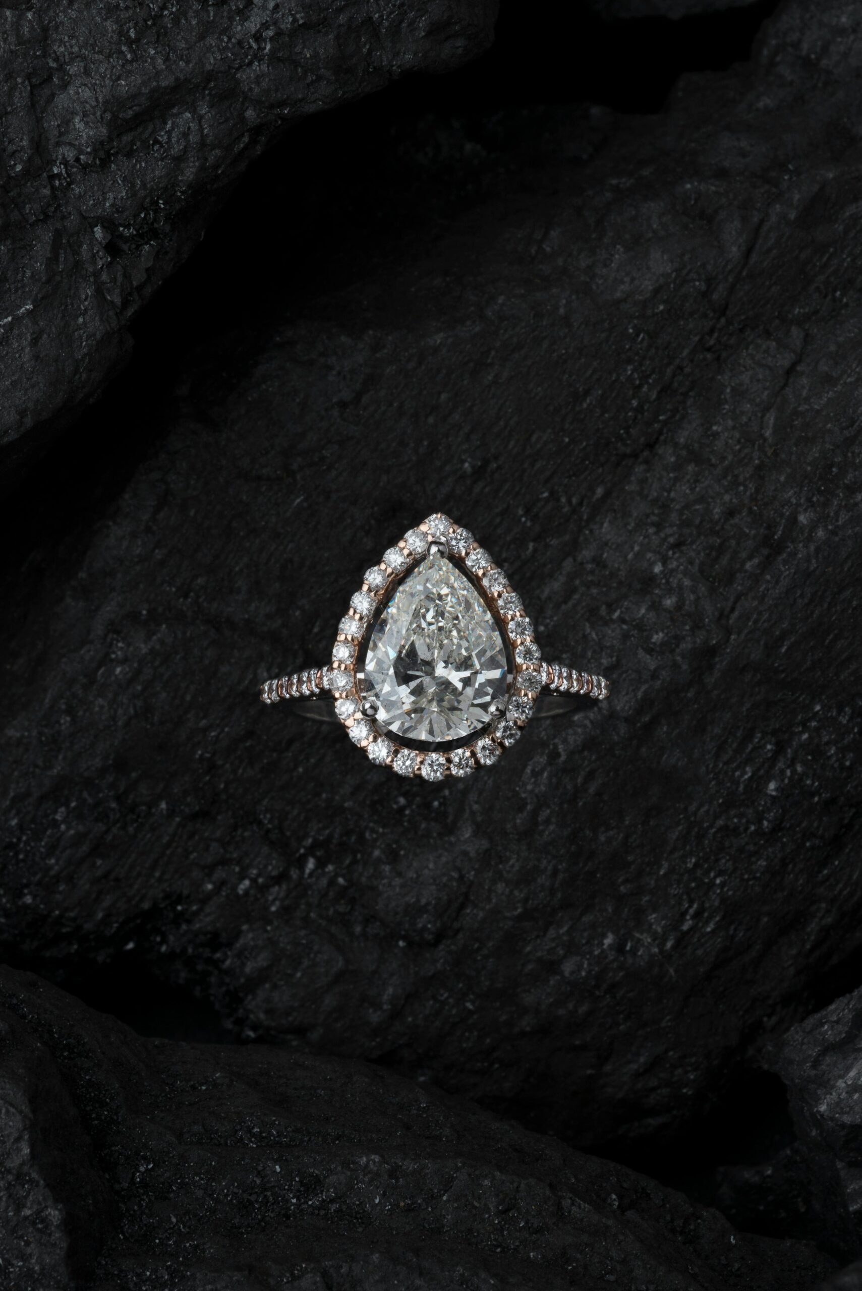 Stunning teardrop diamond ring surrounded by smaller stones on a textured dark background.